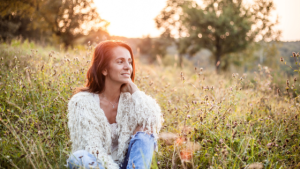 Femme souriante assise dans un champ de fleurs au coucher du soleil