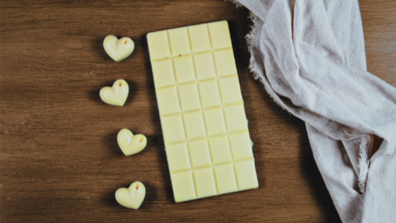 Barre de chocolat blanc et petits chocolats blancs en forme de cœur sur une table en bois