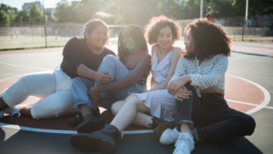 Quatre jeunes femmes assises par terre sur un terrain de basket ball extérieur