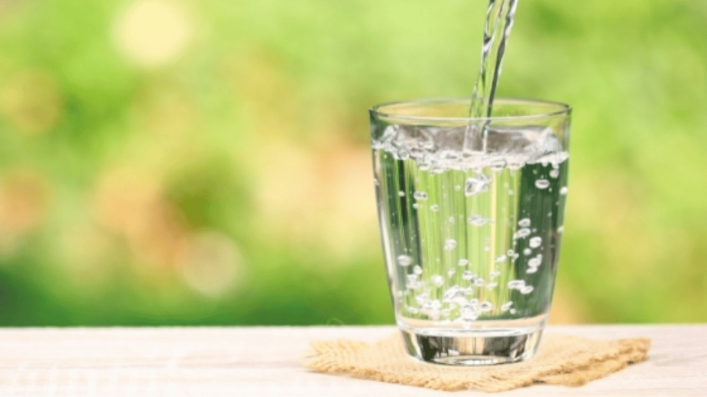 Verre en gros plan sur un sous-verre en jute, qui se fait remplir d'eau sur fond vert.