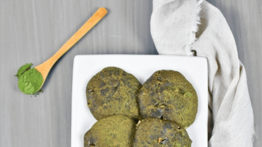 Biscuits « matcha » à la lentille d’eau verdâtre dans une assiette blanche avec une cuiller en bois contenant de la poudre de matcha