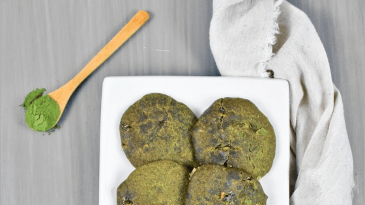 Biscuits « matcha » à la lentille d’eau verdâtre dans une assiette blanche avec une cuiller en bois contenant de la poudre de matcha