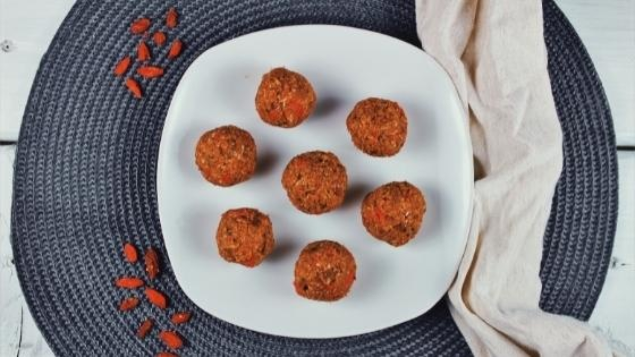 Boules d'énergie déposées dans une assiette blanche sur un napperon gris et des baies de goji en décoration