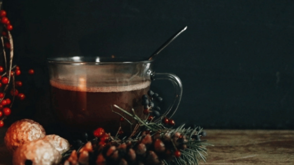 Tasse de boisson chaude décorée avec des tiges de sapin, une cocotte de pin et des petites boules rouges évoquant le temps des fêtes