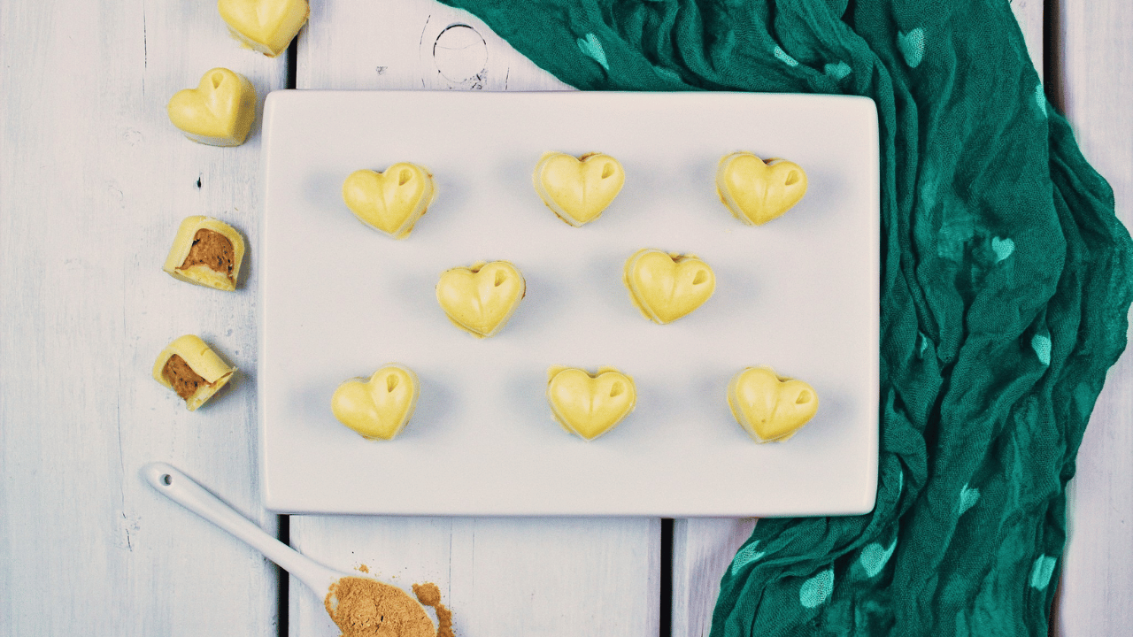 Chocolats blancs en forme de cœur dans une assiette blanche et une cuillère blanche avec de la poudre de maca dorée